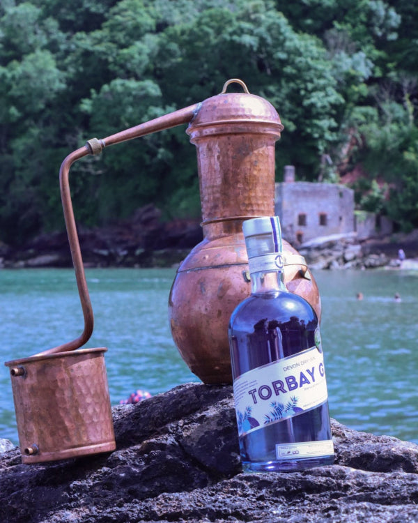 Torbay Gin bottle in front of a copper still at Elberry Cove